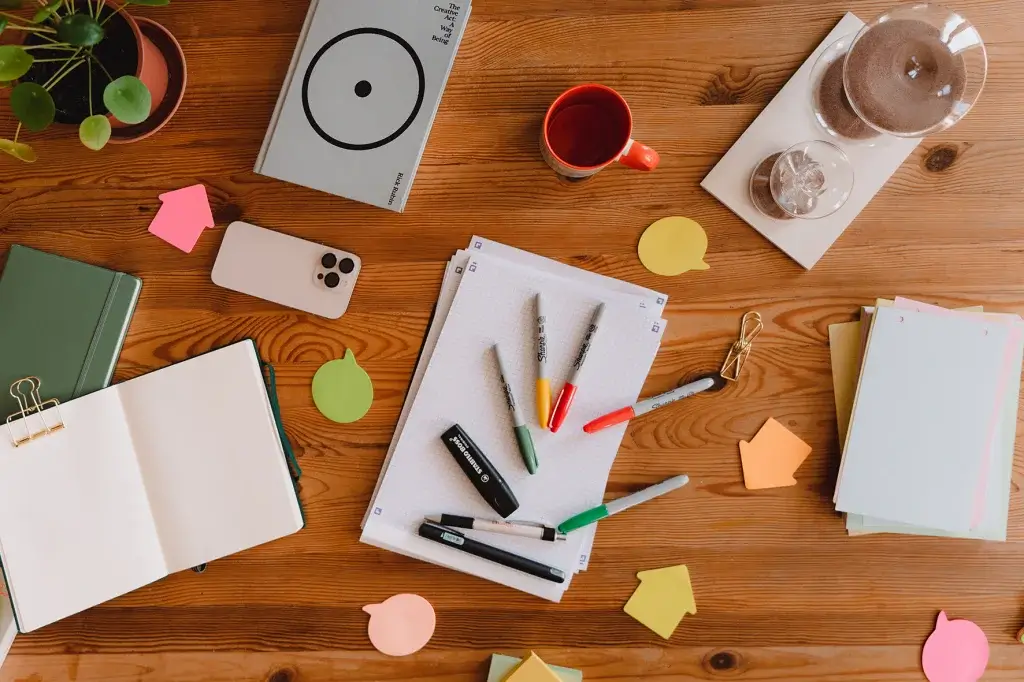 Photo of a table from above containing notebooks, pens, sticky notes, coffee cups.